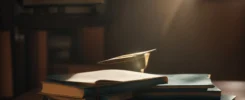a stack of college textbooks beside a graduation cap, with a bright light shining on them from above.