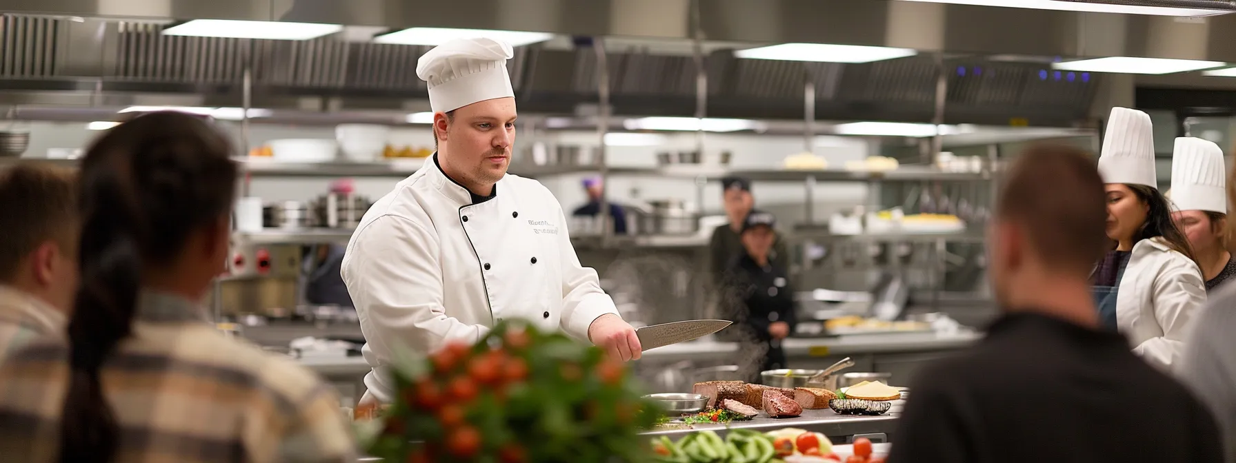 a chef demonstrating knife skills in a virtual cooking class with students watching attentively.